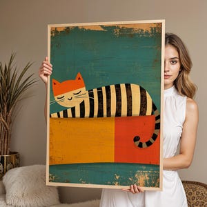 Puede incluir: Un cuadro enmarcado con una ilustración de un gato estilizado. El gato, con orejas naranjas y cuerpo a rayas, descansa sobre un fondo colorido de color turquesa, amarillo y rojo. La obra de arte tiene un aspecto vintage y texturizado, y se presenta en un marco de madera.