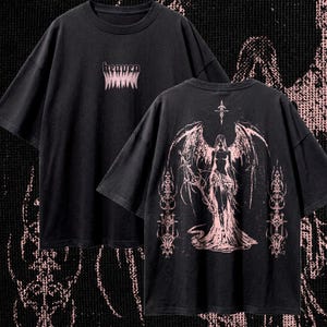 May include: Black t-shirt with the word "heaven" in pink, above a jagged design. The back of the shirt features a pink illustration of an angel with large wings and ornate details. The shirt has a vintage, distressed look.
