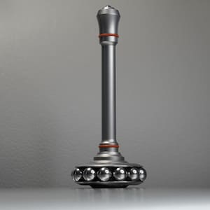 May include: A silver-colored metal desk toy with a long, cylindrical stem and a rounded base containing six small, shiny spheres. The top of the toy has a decorative, rounded design. A thin, orange ring accents the stem.