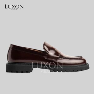Może przedstawiać: Para bordowych sk&oacute;rzanych mokasyn&oacute;w z grubą czarną podeszwą. Buty mają klasyczny design penny loafer z błyszczącym wykończeniem. Nazwa marki "LUXON CRAFTS" jest wydrukowana w lewym g&oacute;rnym i prawym dolnym rogu obrazu.