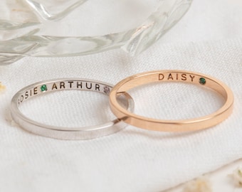 May include: Two thin gold and silver rings with the names "Daisy" and "Rosie Arthur" engraved on them. Each ring has a small green gemstone.