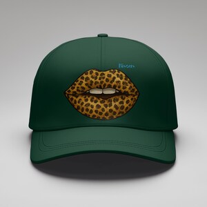 Peut inclure: Casquette de baseball vert foncé avec un motif de lèvres léopard. Les lèvres sont marron et beige avec des dents blanches. Le mot "Bisous" est écrit en bleu clair au-dessus des lèvres. La casquette a une visière incurvée.