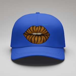 Könnte beinhalten: Eine königsblaue Baseballkappe mit einer Grafik von Lippen mit einem braunen und schwarzen Streifenmuster. Das Wort "Bisous" ist hellblau auf der Kappe geschrieben.