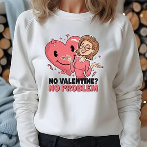 以下が含まれることがあります： 白いスウェットシャツに、ピンクの漫画のハートと眼鏡をかけた女性が描かれています。スウェットシャツには「NO VALENTINE? NO PROBLEM.」という文字が書かれています。