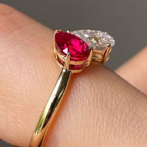 May include: A gold ring featuring two pear-shaped gemstones: a vibrant red ruby and a clear, sparkling diamond. The ring's band is a polished gold, and the gemstones are set close together, creating a unique and elegant design.