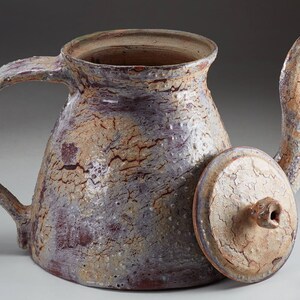 May include: A ceramic teapot with a lid, the teapot is a light brown color with a crackled glaze, the lid is a light brown color with a crackled glaze and a small spout on top