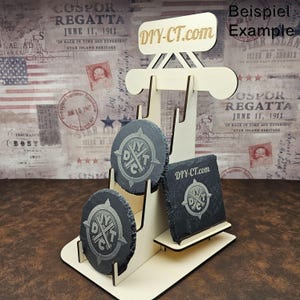 Könnte beinhalten: Ein Holzständer mit drei Ebenen zum Präsentieren von runden Untersetzern. Die Untersetzer sind aus schwarzem Schiefer und zeigen ein weißes Logo mit dem Text "DIY-CT.com".