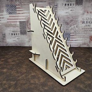 May include: A light-colored wooden display stand featuring a series of cut-out chevron patterns along its angled side. The structure includes multiple small hooks along the slanted edge and a flat base, designed for organizing and holding items.