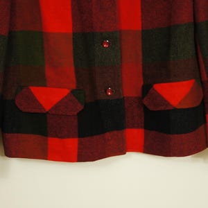May include: A red, black, and green plaid jacket with two front pockets and two red buttons. The jacket has a classic lumberjack style, with a bold, eye-catching pattern. The fabric appears to be a thick wool or wool blend.