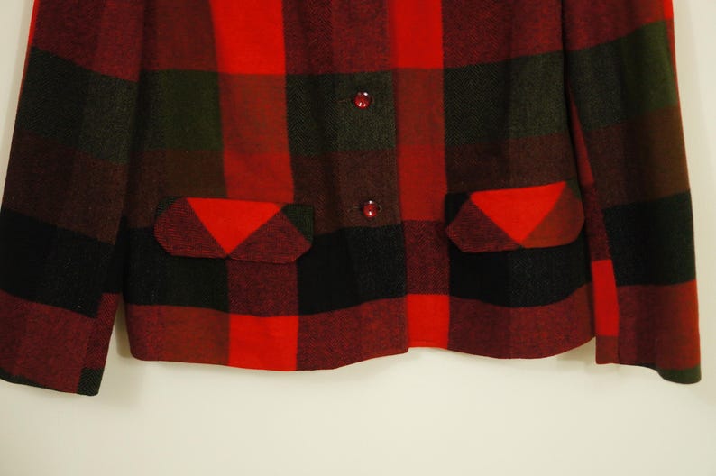May include: A red, black, and green plaid jacket with two front pockets and two red buttons. The jacket has a classic lumberjack style, with a bold, eye-catching pattern. The fabric appears to be a thick wool or wool blend.