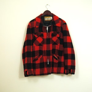 May include: A red and black plaid jacket with a full zipper closure and two front pockets. The jacket is hanging on a wooden hanger against a white wall. The jacket has a collar and a label that reads "Quality Outerwear".