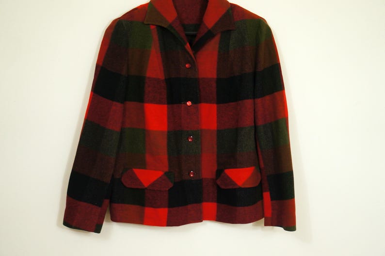 May include: A red, black, and green plaid jacket with a collared neckline and three red buttons. The jacket has two front pockets and is made of a thick, warm material.