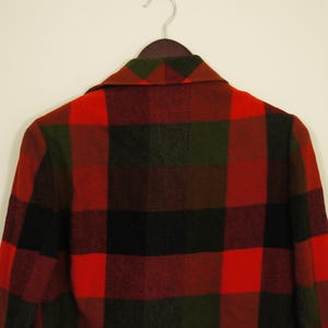 May include: A red, black, and green plaid jacket hanging on a wooden hanger. The jacket has a classic lumberjack pattern, with large, bold squares of color. The collar is visible, and the jacket appears to be made of a thick, warm material.
