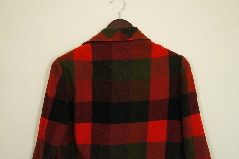 May include: A red, black, and green plaid jacket hanging on a wooden hanger. The jacket has a classic lumberjack pattern, with large, bold squares of color. The collar is visible, and the jacket appears to be made of a thick, warm material.