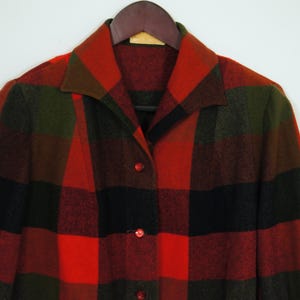 May include: A vintage, button-down coat in a bold plaid pattern of red, black, and olive green. The coat features a classic collar and is displayed on a wooden hanger. The fabric appears to be a warm, wool blend.