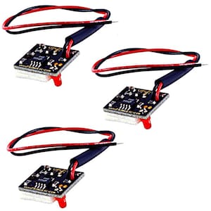 May include: Three small black circuit boards with red and black wires attached. Each board has a red LED and is mounted on a white base. The wires are encased in black tubing. The boards are likely electronic components.