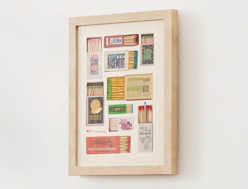 May include: A framed collage of matchboxes with various designs and text, including "Welcome Back to the Basement", "Dog Sniffin' Season", and "Put it on the Blendah".