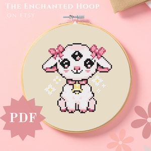 May include: A cross-stitch pattern featuring a cute, cartoon lamb with three eyes, pink bows, and a bell around its neck. The pattern is in a white embroidery hoop on a pink background. The text "PDF" is on a pink starburst.