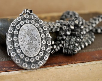 May include: A silver locket with a floral design and a chain. The locket is surrounded by a border of stars.