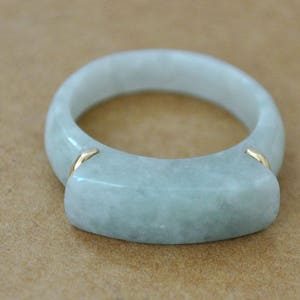 May include: A light green jade ring with gold accents. The ring is a simple band with a flat top.