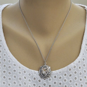 May include: A silver chain necklace with a silver pendant featuring a circular design with gears and a butterfly inside.