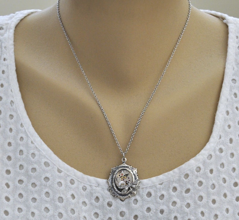 May include: A silver chain necklace with a silver pendant featuring a circular design with gears and a butterfly inside.