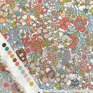May include: A white fabric with a colorful floral pattern featuring strawberries, mushrooms, and cartoon characters. The fabric has a fringed edge and a color swatch card.