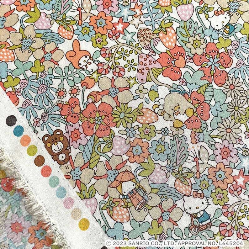 May include: A white fabric with a colorful floral pattern featuring strawberries, mushrooms, and cartoon characters. The fabric has a fringed edge and a color swatch card.