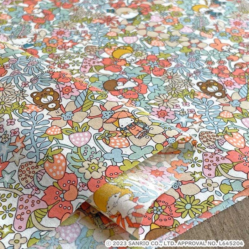 May include: A white fabric with a repeating pattern of pink, red, and blue flowers, strawberries, mushrooms, and stars. The fabric features a cartoon character with a red hat and a brown bear.