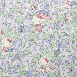 May include: A white fabric with a repeating pattern of blue flowers and cartoon characters. The characters are wearing pink and blue clothing and holding umbrellas and watering cans.