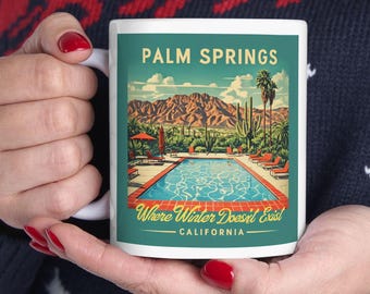 Op de afbeelding: Witte keramische mok met een retro-illustratie van een zwembad en bergen. De tekst "PALM SPRINGS" staat in een vet, geel lettertype. Onder de afbeelding staat de tekst "Where Winter Doesn't Exist - CALIFORNIA - "