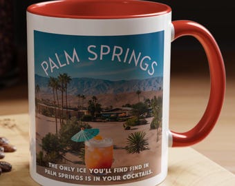 Op de afbeelding: Een witte keramische mok met een rode rand en handvat. De mok heeft een kleurrijk beeld van een woestijnlandschap met palmbomen en een cocktail met een paraplu. De tekst "PALM SPRINGS" staat in grote, vetgedrukte letters bovenaan de mok. De tekst "THE ONLY ICE YOU'LL FIND IN PALM SPRINGS IS IN YOUR COCKTAILS." staat onderaan de mok.