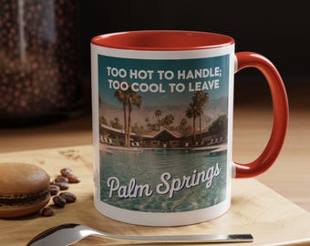 Op de afbeelding: Witte keramische mok met een rode rand en handvat. De mok heeft een retro-afbeelding van een zwembad en palmbomen met de tekst "Too hot to handle; too cool to leave Palm Springs".