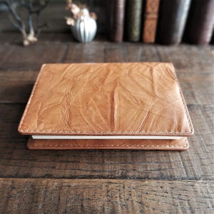 May include: A rectangular notebook with a light brown, textured cover featuring a distinct wrinkled pattern. The cover has visible stitching along the edges, and the white pages of the notebook are visible between the top and bottom covers.