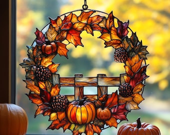 Op de afbeelding: Een gebrandschilderde krans met herfstbladeren in oranje, rood en geel, met pompoenen en dennenappels. De krans hangt voor een raam. Twee pompoenen staan op de vensterbank.
