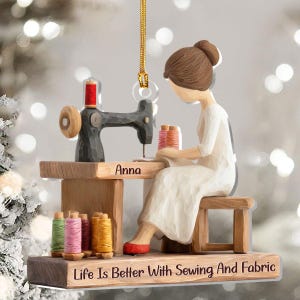 May include: A wooden ornament depicting a person sewing at a sewing machine. The ornament features spools of thread in various colors, the name "Anna", and the text "Life Is Better With Sewing And Fabric".