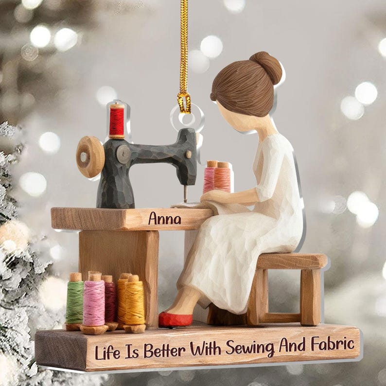 May include: A wooden ornament depicting a person sewing at a sewing machine. The ornament features spools of thread in various colors, the name "Anna", and the text "Life Is Better With Sewing And Fabric".