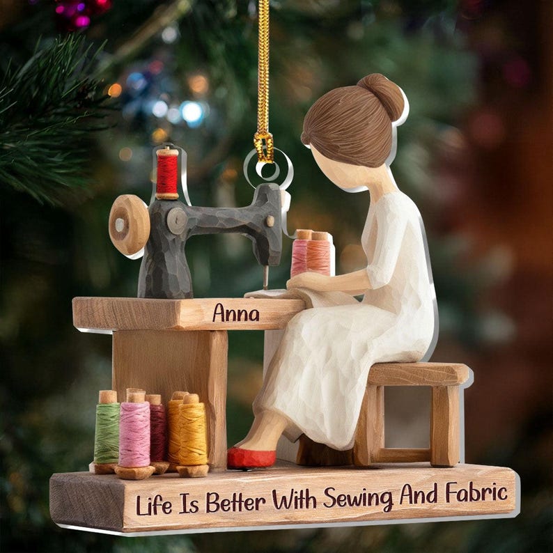 May include: A wooden ornament depicting a person sewing at a vintage sewing machine. The ornament features spools of thread in various colors, the name "Anna", and the text "Life Is Better With Sewing And Fabric". The person is wearing a white dress and red shoes.