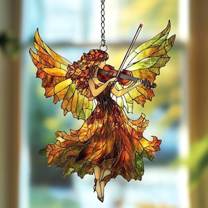 Puede incluir: Hada de vidriera tocando el violín, con alas y un vestido en tonos naranja, amarillo y verde. El hada está suspendida por una cadena, adecuada para colgar. El diseño presenta detalles intrincados y un tema inspirado en la naturaleza.