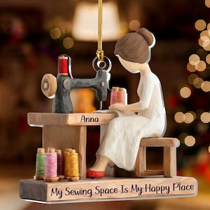 May include: A wooden ornament depicting a person sewing at a sewing machine. The ornament features a person in a white dress, a black sewing machine, and spools of thread in various colors. The text "Anna" and "My Sewing Space Is My Happy Place" are visible.