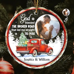 Puede incluir: Adorno navideño personalizado con un camión rojo que transporta un árbol de Navidad y regalos. El adorno presenta una foto de una pareja besándose, con el texto "Dios bendijo el camino roto que me llevó directamente a ti". Los nombres "Sophia & William" también están incluidos.