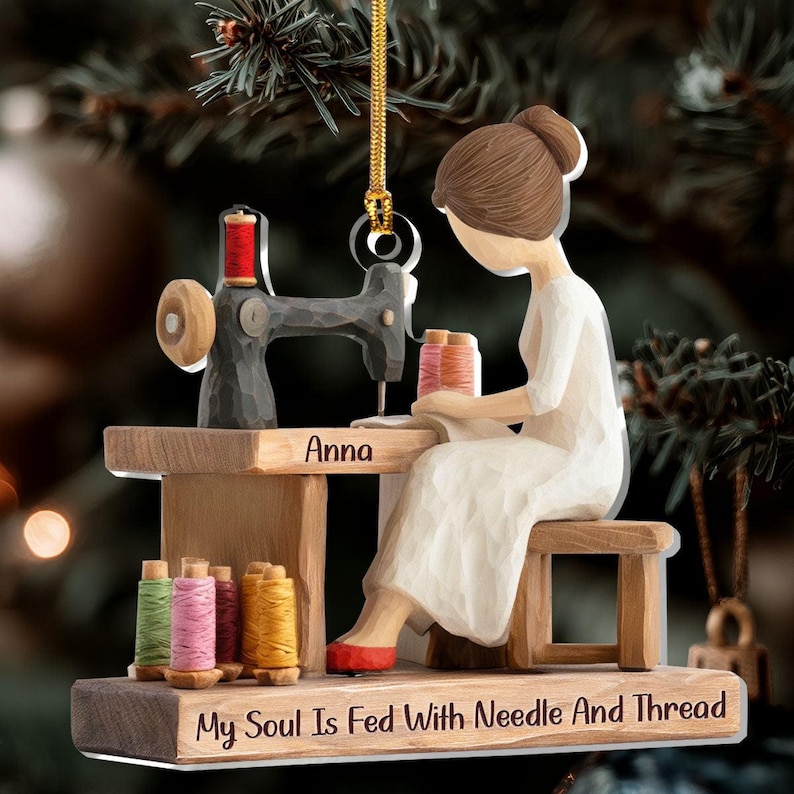 May include: A wooden Christmas ornament depicting a person sewing at a sewing machine. The ornament features the name "Anna" and the text "My Soul Is Fed With Needle And Thread". The ornament includes spools of thread in various colors.