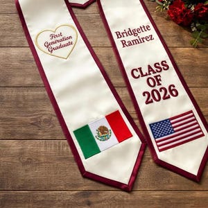 May include: Two graduation stoles with white fabric and burgundy trim. One stole has the text "First Generation Graduate" in a heart, and the Mexican flag. The other stole has the name "Bridgette Ramirez", the text "CLASS OF 2026", and the American flag.