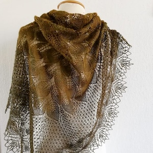 Puede incluir: Un chal de encaje verde oliva delicado con un patrón de encaje intrincado. El chal está drapeado sobre un maniquí blanco.