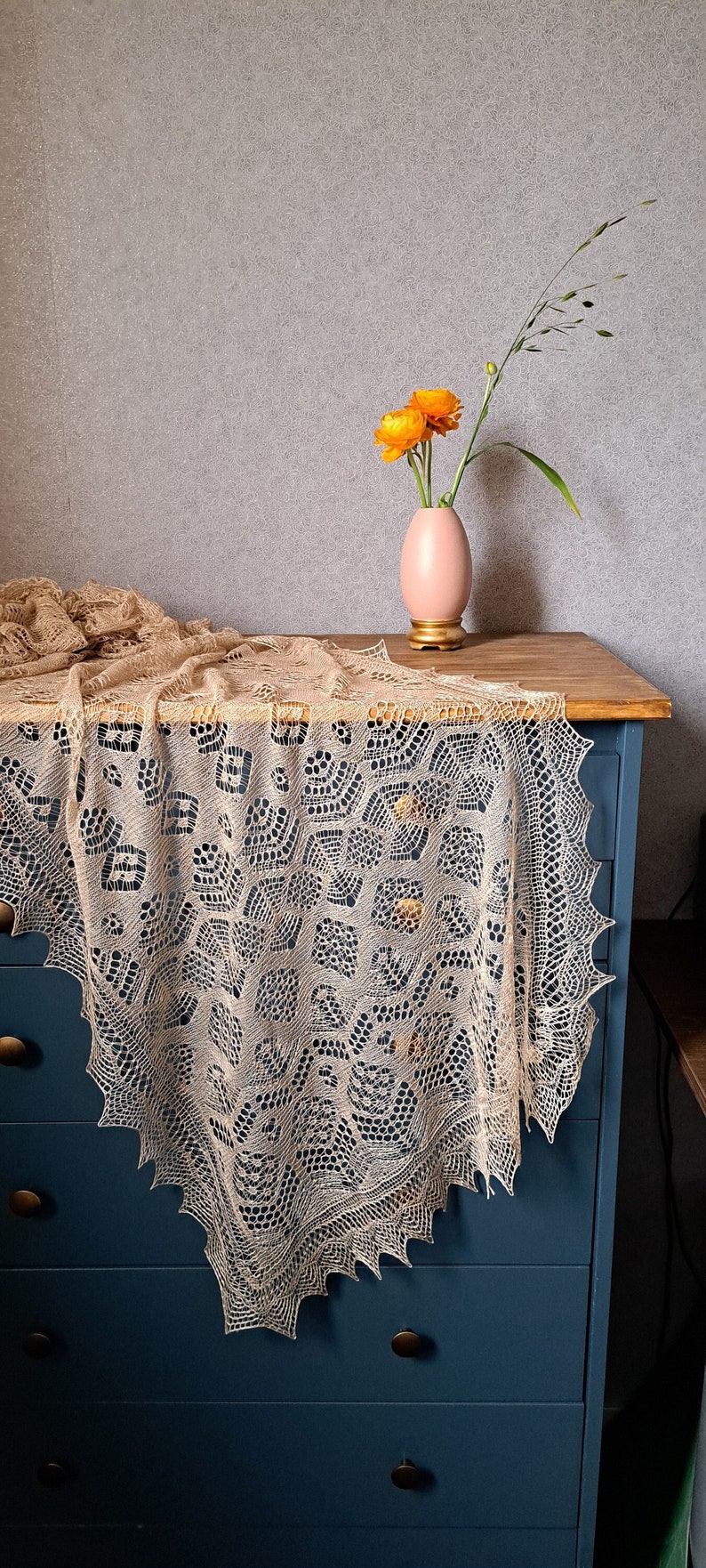 A beige silk lace shawl, draped over a blue drawer. Orange flower arrangement.