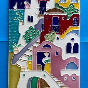 May include: A rectangular ceramic tile featuring a colorful Mediterranean coastal scene with white, red, and pink buildings, a yellow moon in a dark blue starry sky, and two small boats resting on a sandy shore by turquoise water.