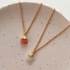 May include: Two gold necklaces with delicate chains and shell pendants. One pendant is a light orange colour and the other is a light blue colour.