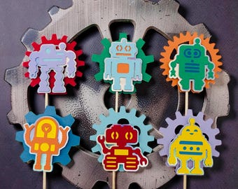 May include: Six colorful robot cupcake toppers on wooden sticks. Each robot is a different color, including blue, green, orange, red, and yellow, and is set against a gear-shaped background. The robots have a cartoonish design.