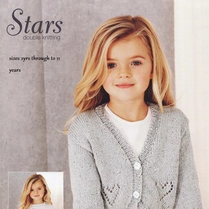 May include: A light gray knitted cardigan with a button closure and a star-shaped design on the front and back. The cardigan is shown on a young girl wearing a white dress. The text "Stars double knitting" and "sizes 2yrs through to 11 years" is visible in the image.