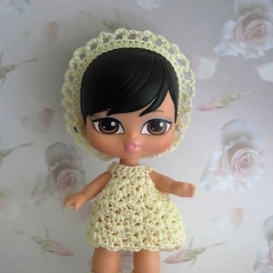May include: A yellow crocheted dress, hat, and shoes for a doll. The doll has black hair and brown eyes.